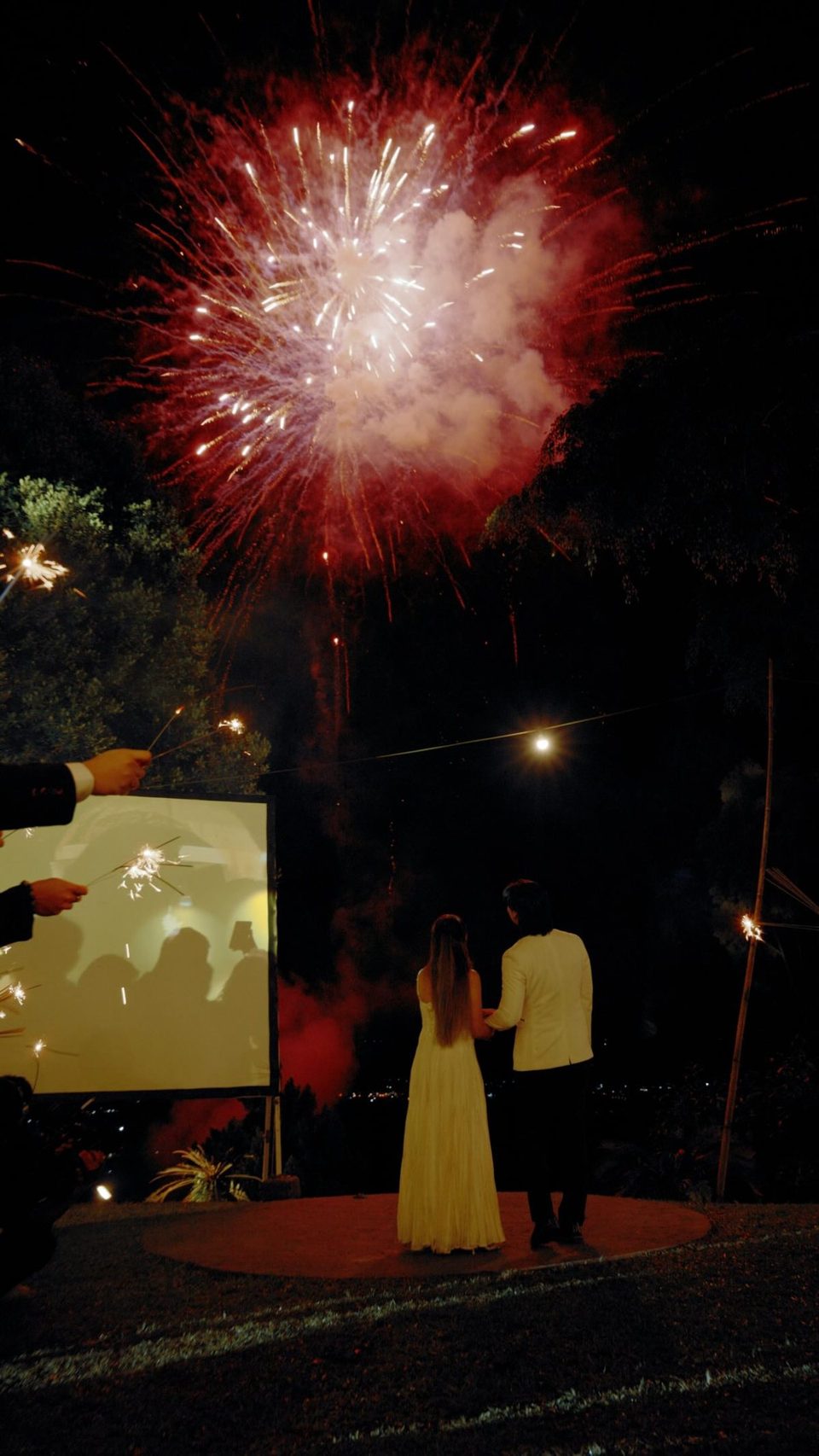 A couple watching fireworks over the hillside at night at Hillside Kokol, guests holding sparklers